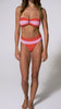 A woman wearing a red and pink striped bandeau bikini spinning in front of a white wall. 