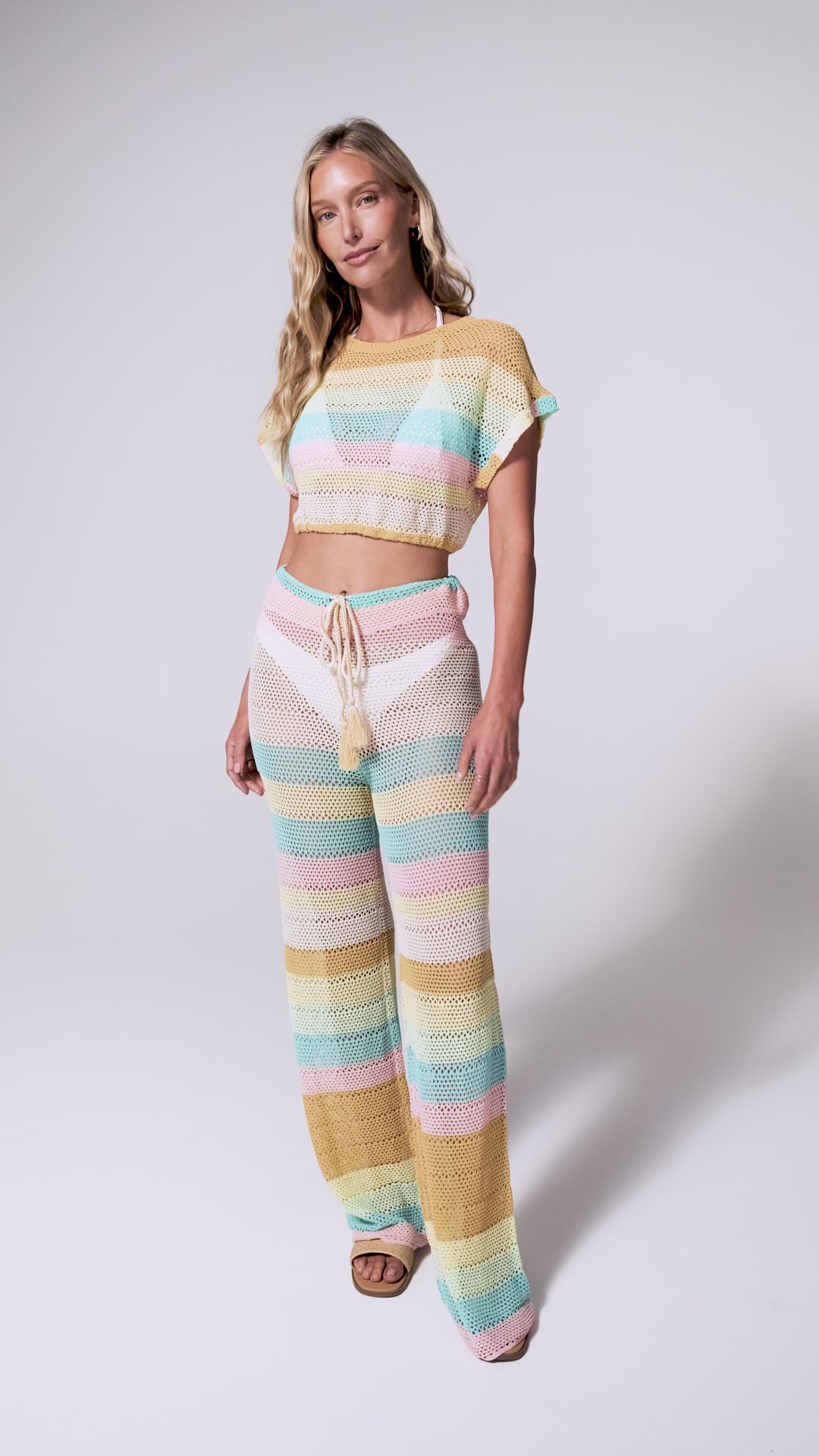 A woman wearing a crochet knit pant and shirt set spinning against a white wall.