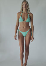 A blonde woman wearing a turquoise bikini spinning in front of a white wall.