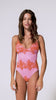 A woman wearing a pink one piece swimsuit with red floral details spinning in front of a white wall. 