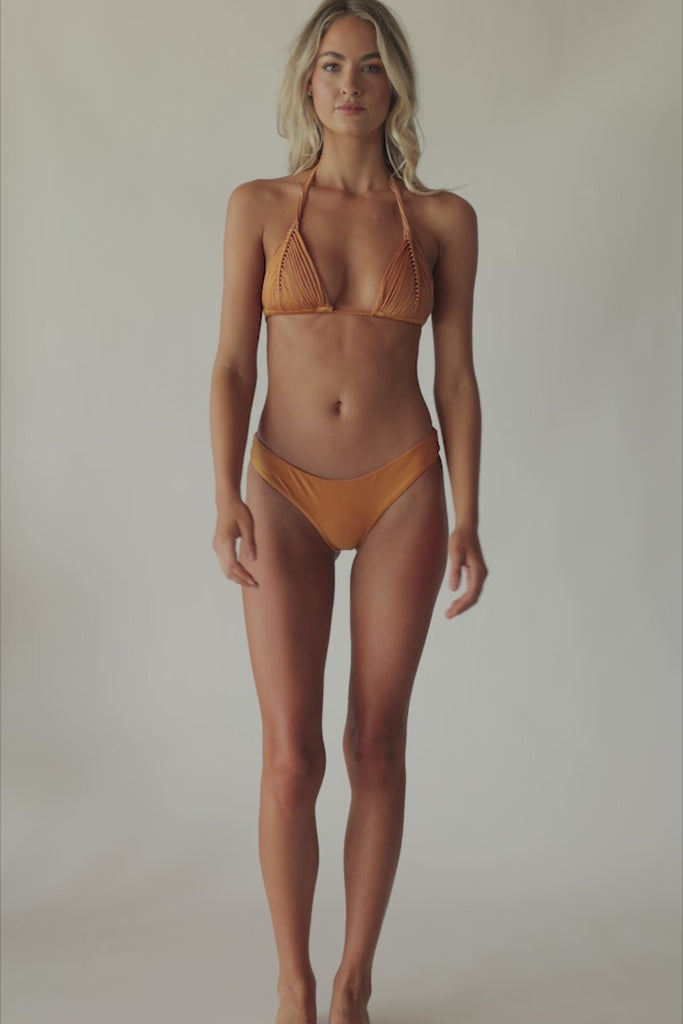 Blonde woman wearing an orange macrame triangle bikini spinning around in front of a white wall.