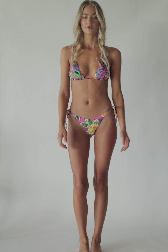 Blonde woman wearing a pink tropical triangle shape bikini with hand-sewn beading spinning around in front of a white wall.