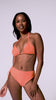 A woman wearing an orange triangle top bikini and matching high waist bottoms spinning in front of a white wall