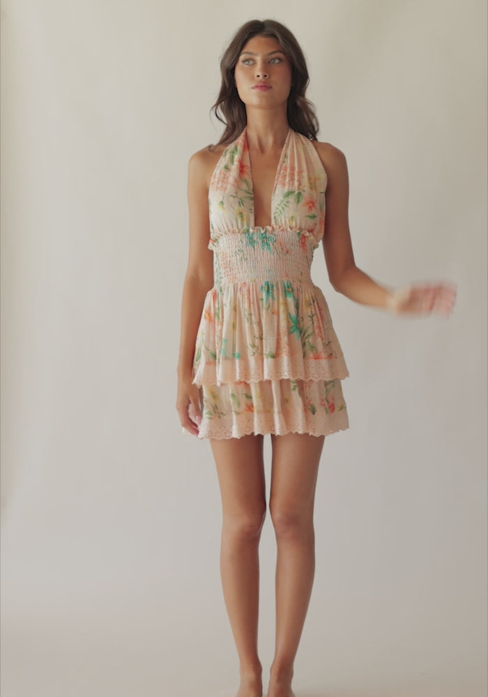 A brunette woman wearing a short tropical dress spinning in front of a white wall.