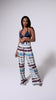 A woman wearing a navy triangle bikini top and blue tie dye pants spinning in front of a white wall.