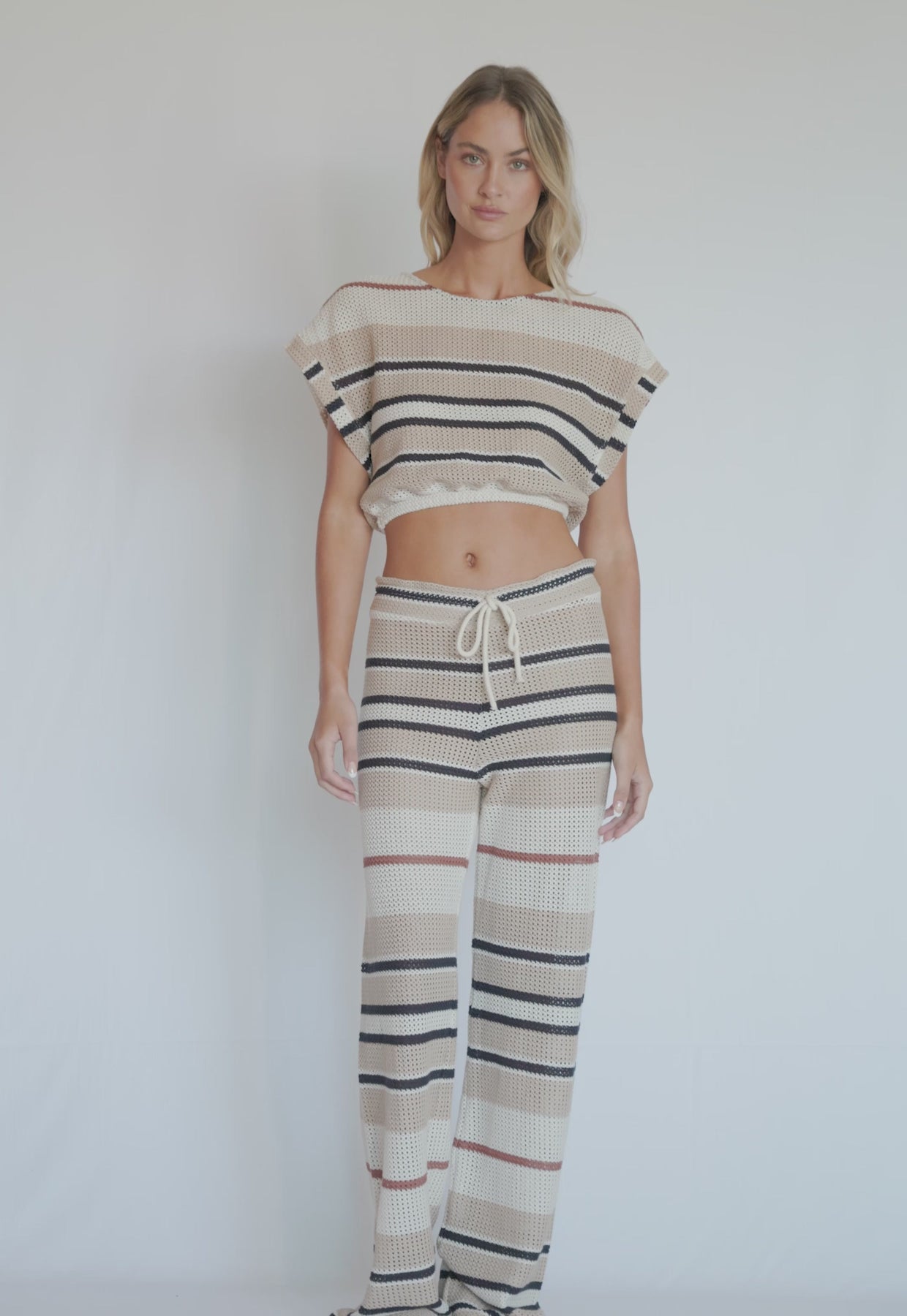 A woman wearing a matching striped crop top and pants spinning in front of a white wall. 