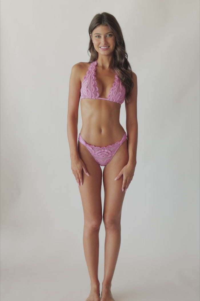 Brunette woman wearing a violet lace halter bikini spinning around in front of a white wall.