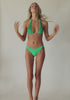 Blonde woman wearing a green halter bikini with net macramé details & shimmery gold accents spinning around in front of a white wall.