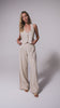 A woman wearing a tan vest and matching linen pants spinning in front of a white wall. 