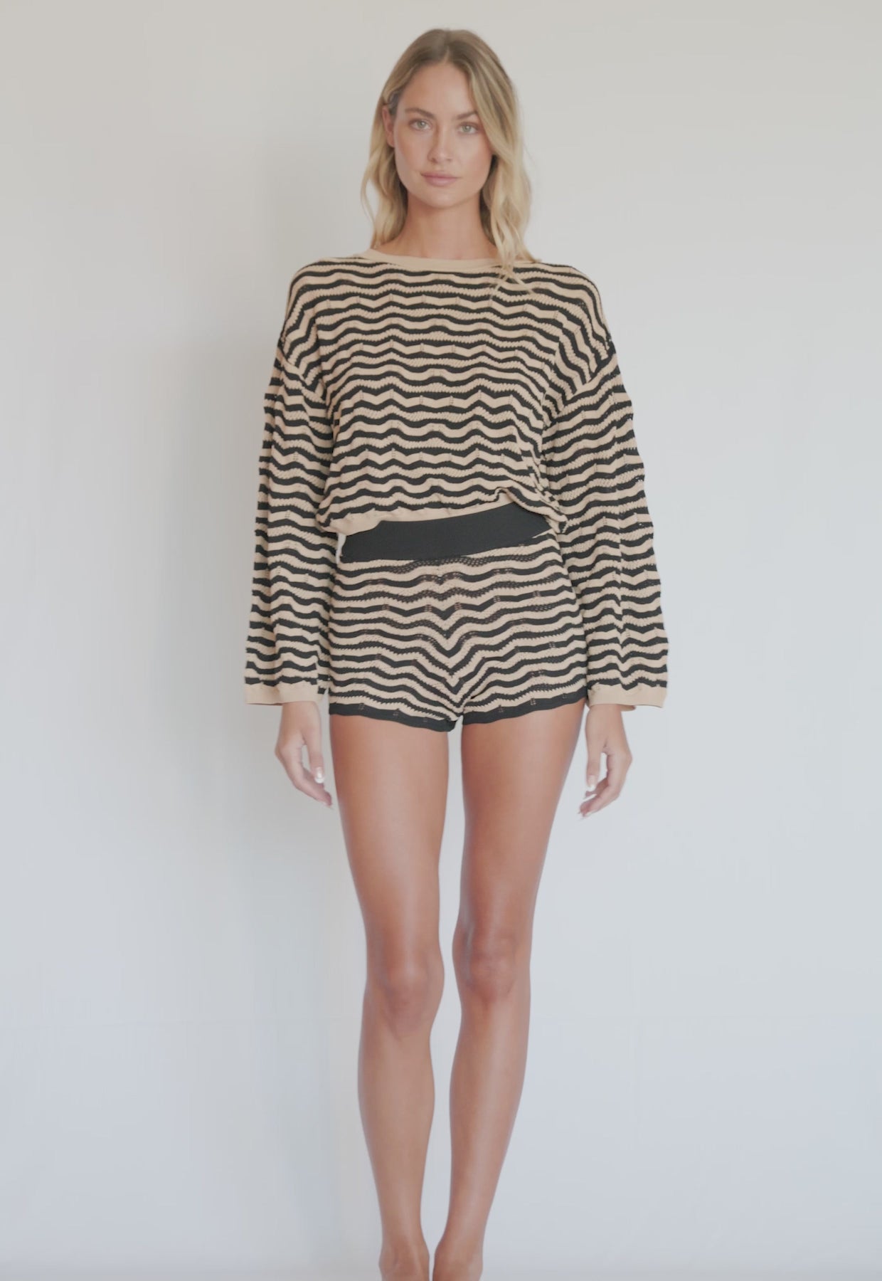 A woman wearing a striped long sleeve top and matching shorts spinning in front of a white wall. 