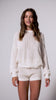 A woman wearing an ivory knit sweater and matching shorts spinning in front of a white wall.