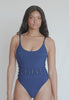 A woman wearing a navy one piece swimsuit spinning in front of a white wall. 