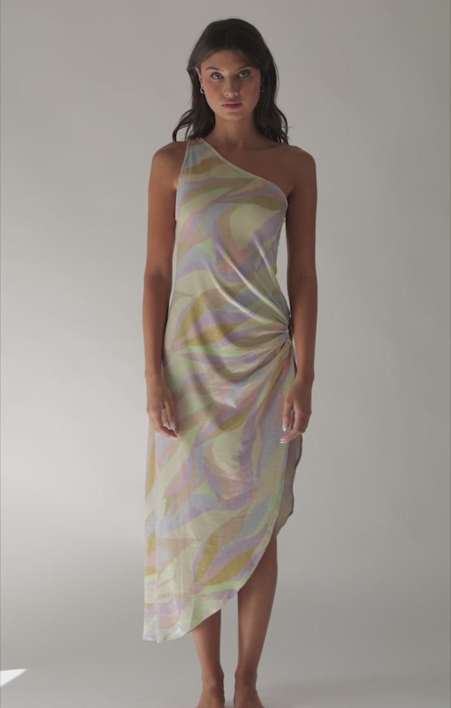 A brunette woman wearing a multi colored dress spinning in front of a white wall. 