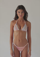 A brunette woman wearing a multi colored bikini spinning in front of a white wall. 