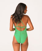A woman wearing a green one piece swimsuit standing against a white wall. 
