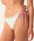 Woman wearing a blue bikini bottom with lace detailing and pink string on a neutral background