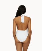 Back view of woman wearing a white one piece in front of a white background. 