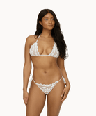 Woman wearing a white lace bikini in front of a white background. 