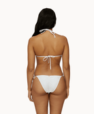 Back view of woman wearing a white lace bikini in front of a white background. 